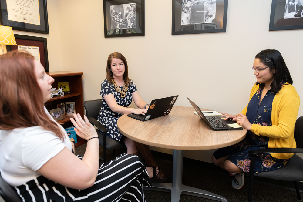 3 staff members sitting together at a round table with their laptops out
